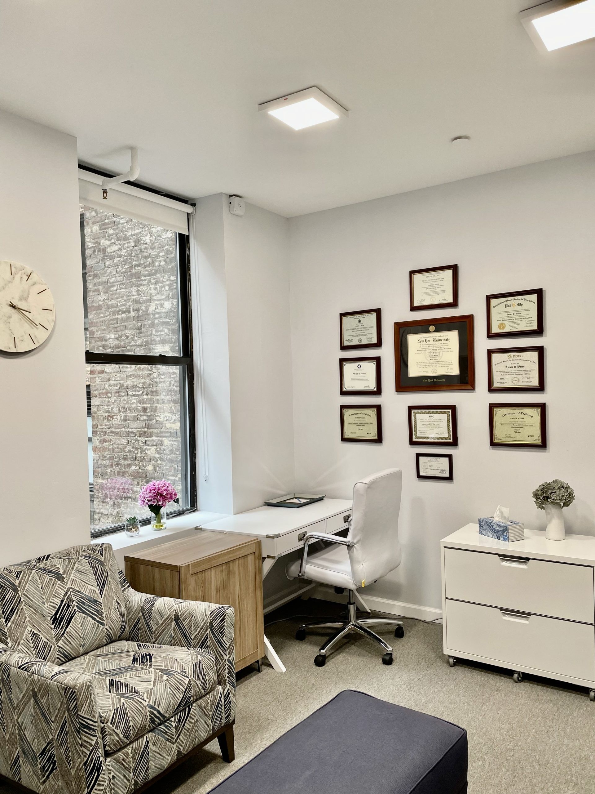 A therapy office with an armchair, a desk and framed diplomas on the wall