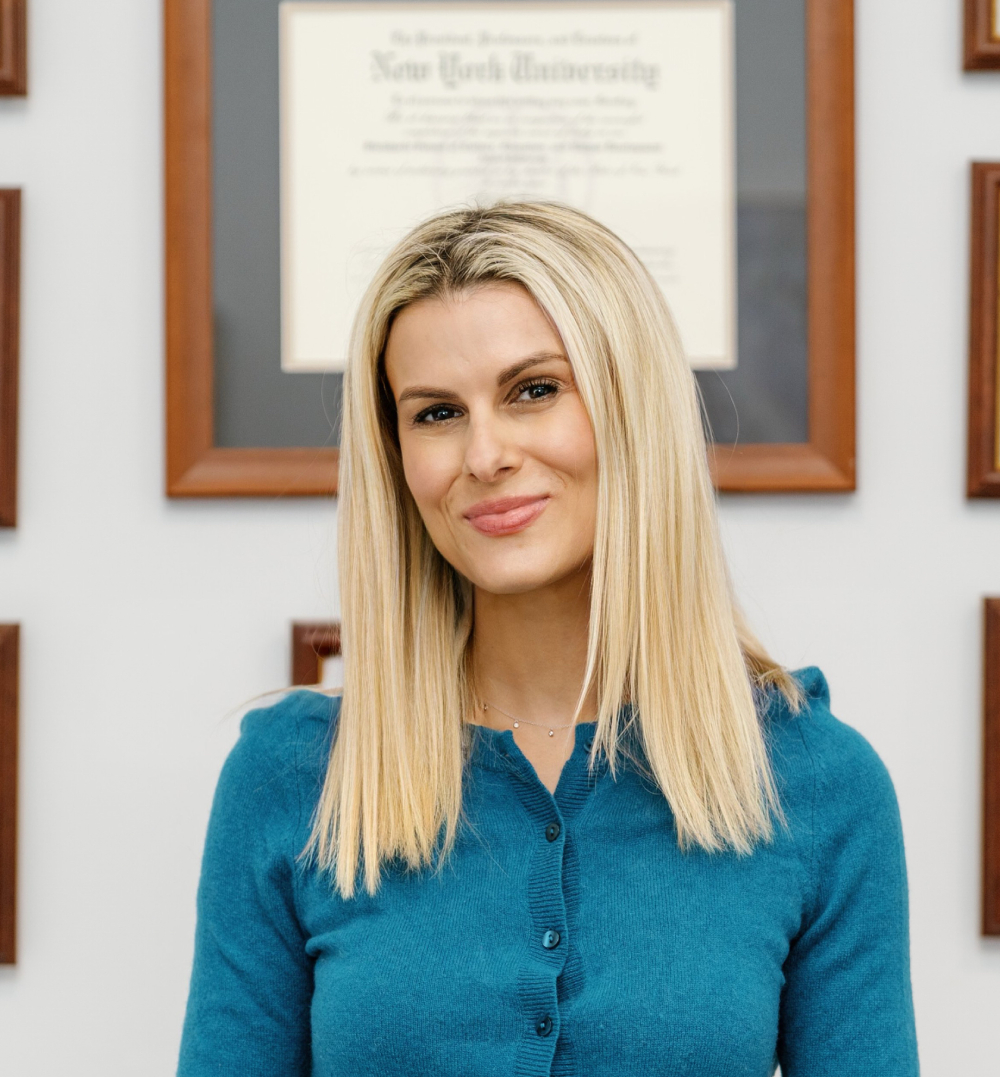 Amber Weiss, founder of Transformative Mindset, wearing a teal cardigan in front of her NYU diploma